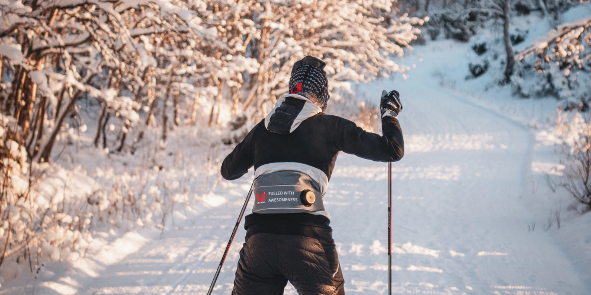 En skidåkare med umarabuff och vätskebälte. åker skidor i solsken.